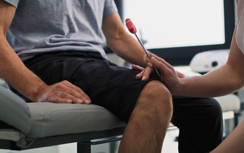 Lekar proverava reflekse pacijenta udarcem čekićem ispod kolena tokom neurološkog pregleda.