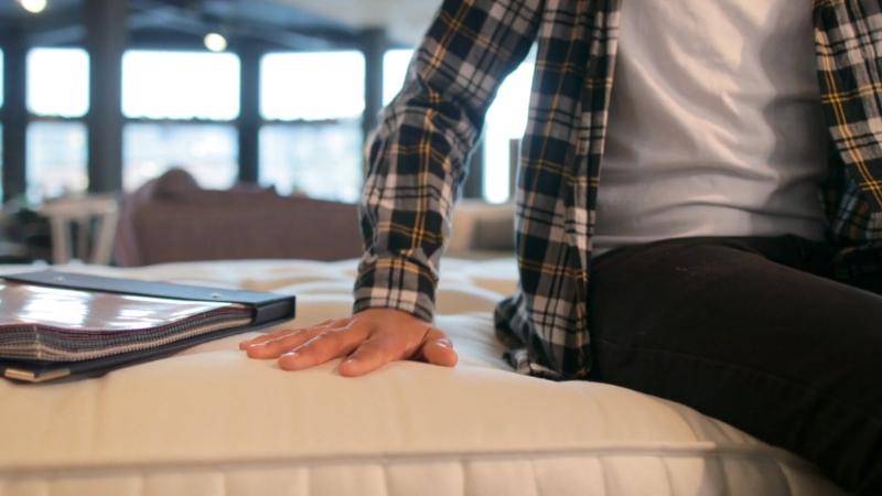 Ruka pritiska dušek u salonu dok kupac procenjuje materijal i tvrdoću na licu mesta