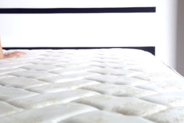 Osoba proverava mekoću svetlog, prošivenog dušeka pre kupovine