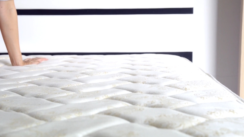 Osoba proverava mekoću svetlog, prošivenog dušeka pre kupovine