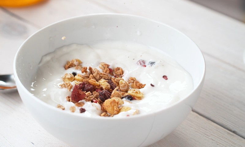Bela činija kremastog jogurta prelivena hrskavom granolom, orasima i sušenim voćem