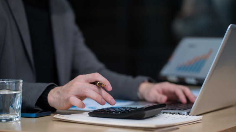 Osoba računa finansije na kalkulatoru uz laptop i poslovne izveštaje