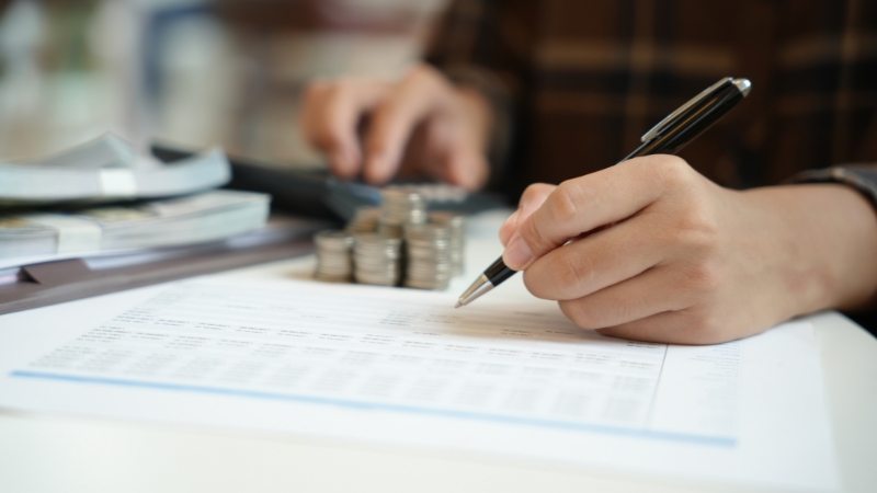 Osoba popunjava finansijski dokument uz novac i kalkulator na stolu