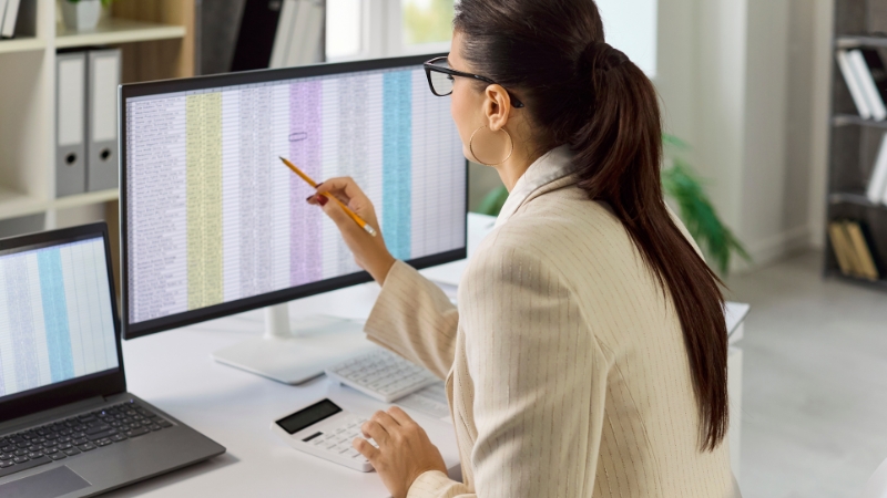 Žena analizira finansijske podatke na velikom ekranu uz računar i dokumentaciju