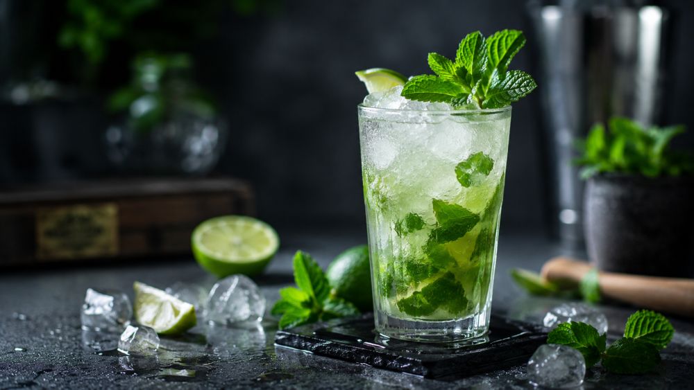 Mojito koktel sa limetom, nanom i drobljenim ledom u visokoj čaši na tamnoj pozadini